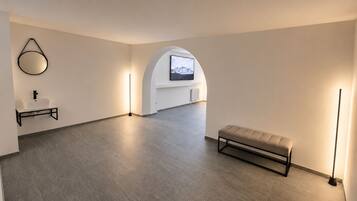 A spacious room with a minimalist design, featuring a bench, a wall-mounted TV, and a floor lamp.
