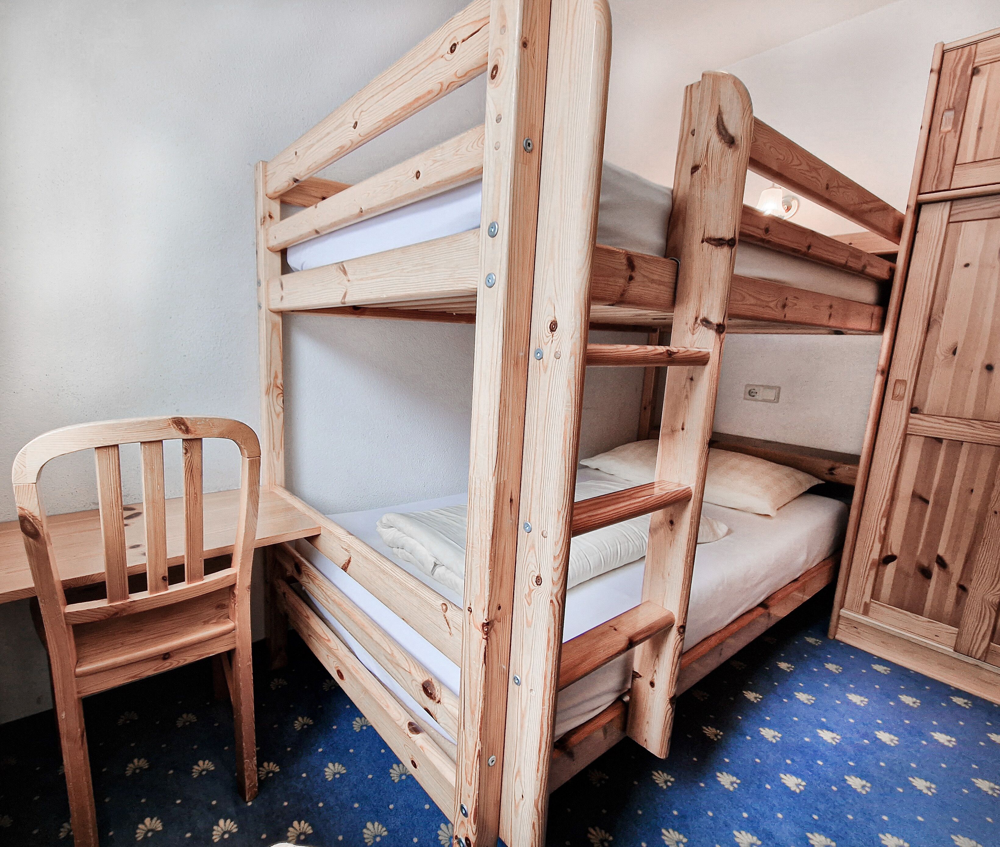 Una cama litera con estructura de madera, una cama individual abajo y una silla de madera.