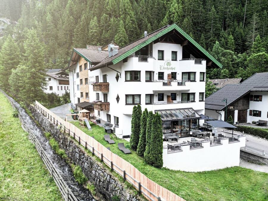 Un hotel de varios pisos con techo verde, zona de estar al aire libre y vistas a una ladera boscosa.