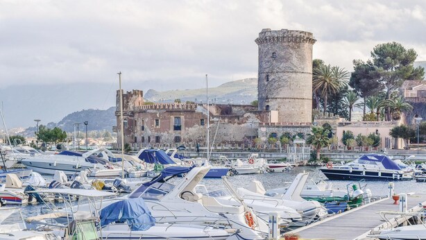 A marina with numerous boats docked, a historic building with a tower, and a mountainous backdrop. - Cozy apartment in San Nicola L'Arena with WiFi (San Nicola L'Arena)