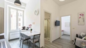 Een moderne keuken met een eettafel en stoelen, een klok aan de muur en een douchegedeelte zichtbaar door een open deur.