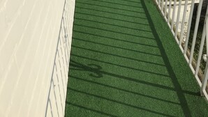 Un balcon doté d’un revêtement de sol vert artificiel, de rampes blanches et offrant une vue sur les bâtiments adjacents.