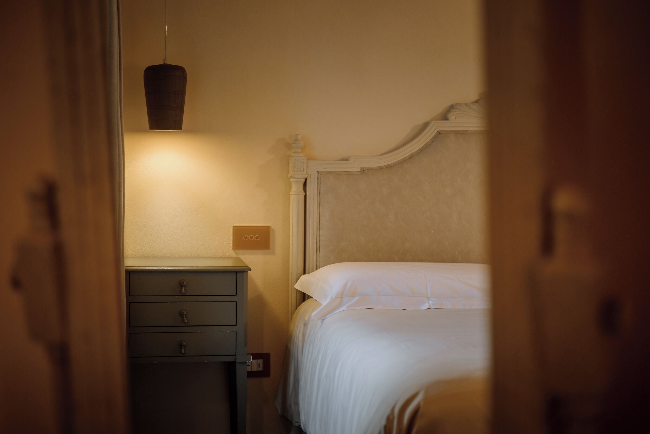 Een slaapkamer met een bed, nachtkastje, lamp en lichtschakelaar.