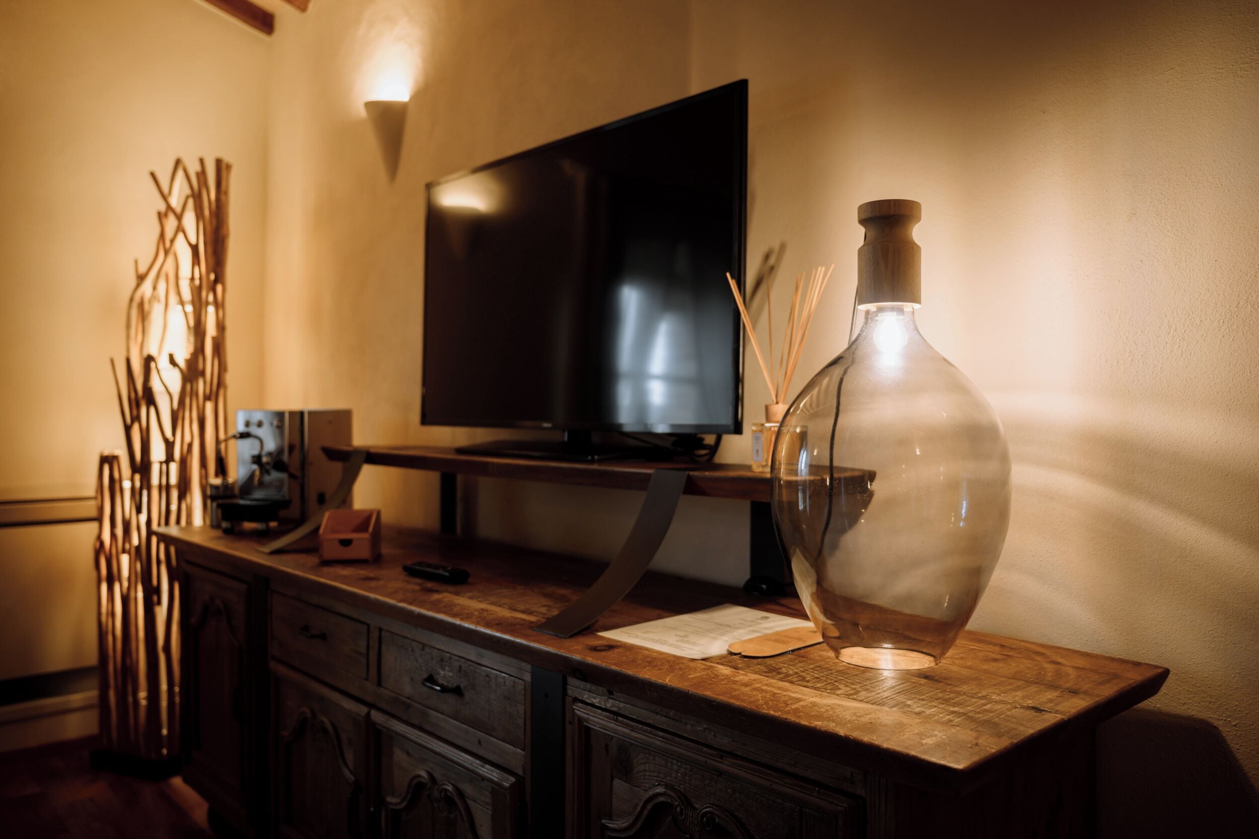 A wooden TV stand with a flat-screen TV, a glass bottle, and decorative branches.