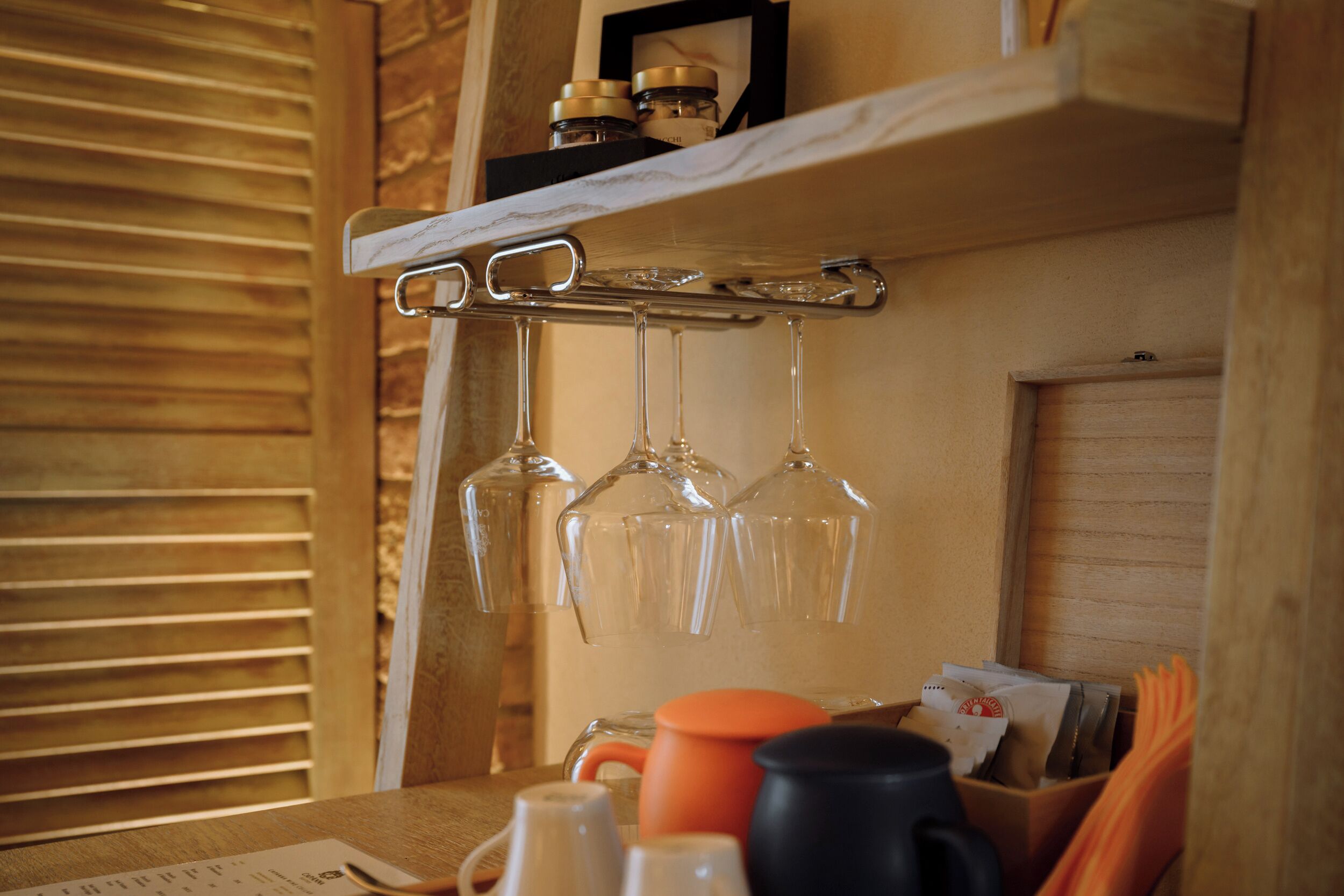 Un intérieur en bois avec une étagère où sont posés des verres à vin, une machine à café et une tasse.