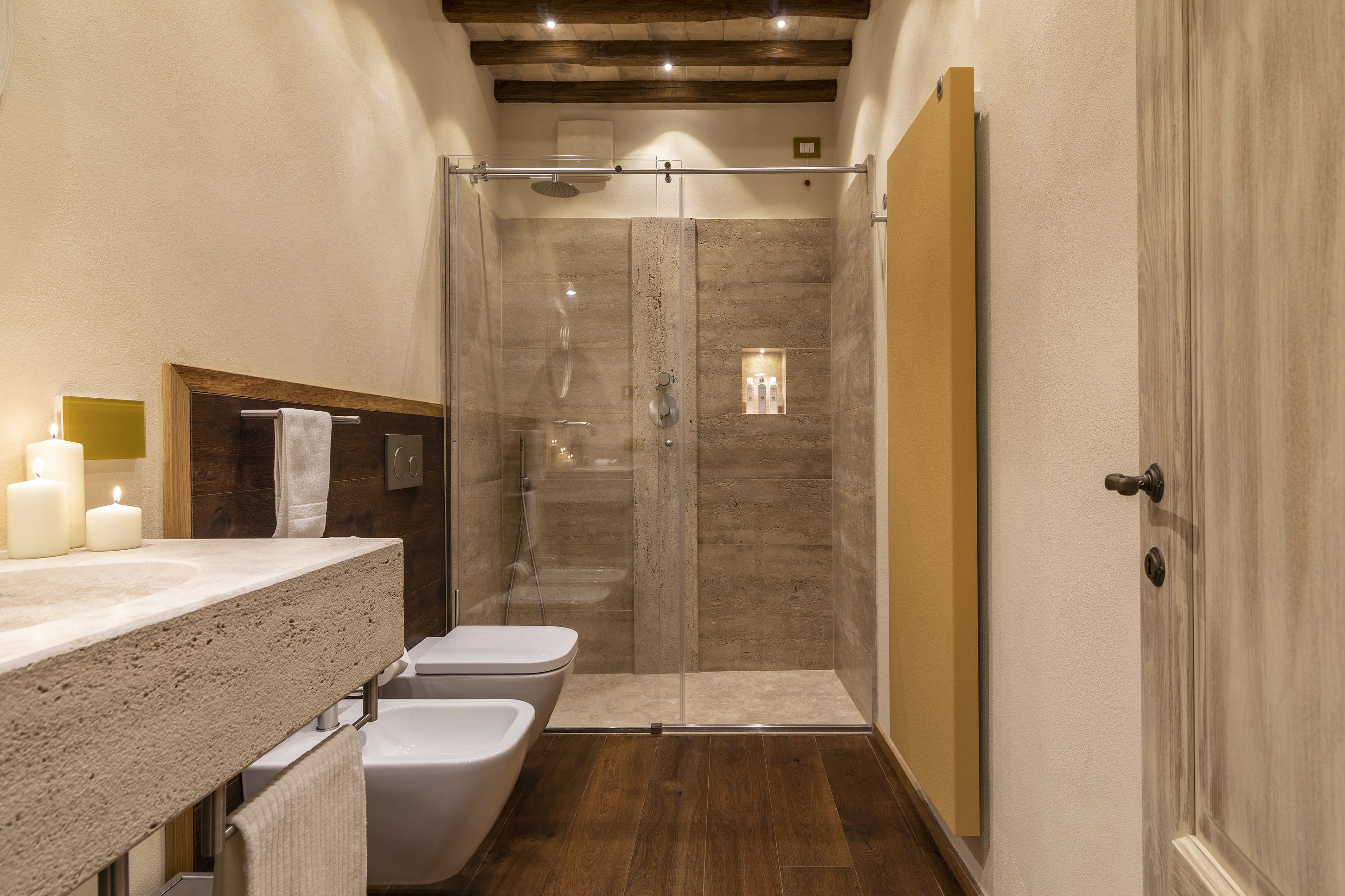 Une salle de bain dotée d’une douche à parois de verre, d’un plafond en bois et d’un sol carrelé de couleur beige.