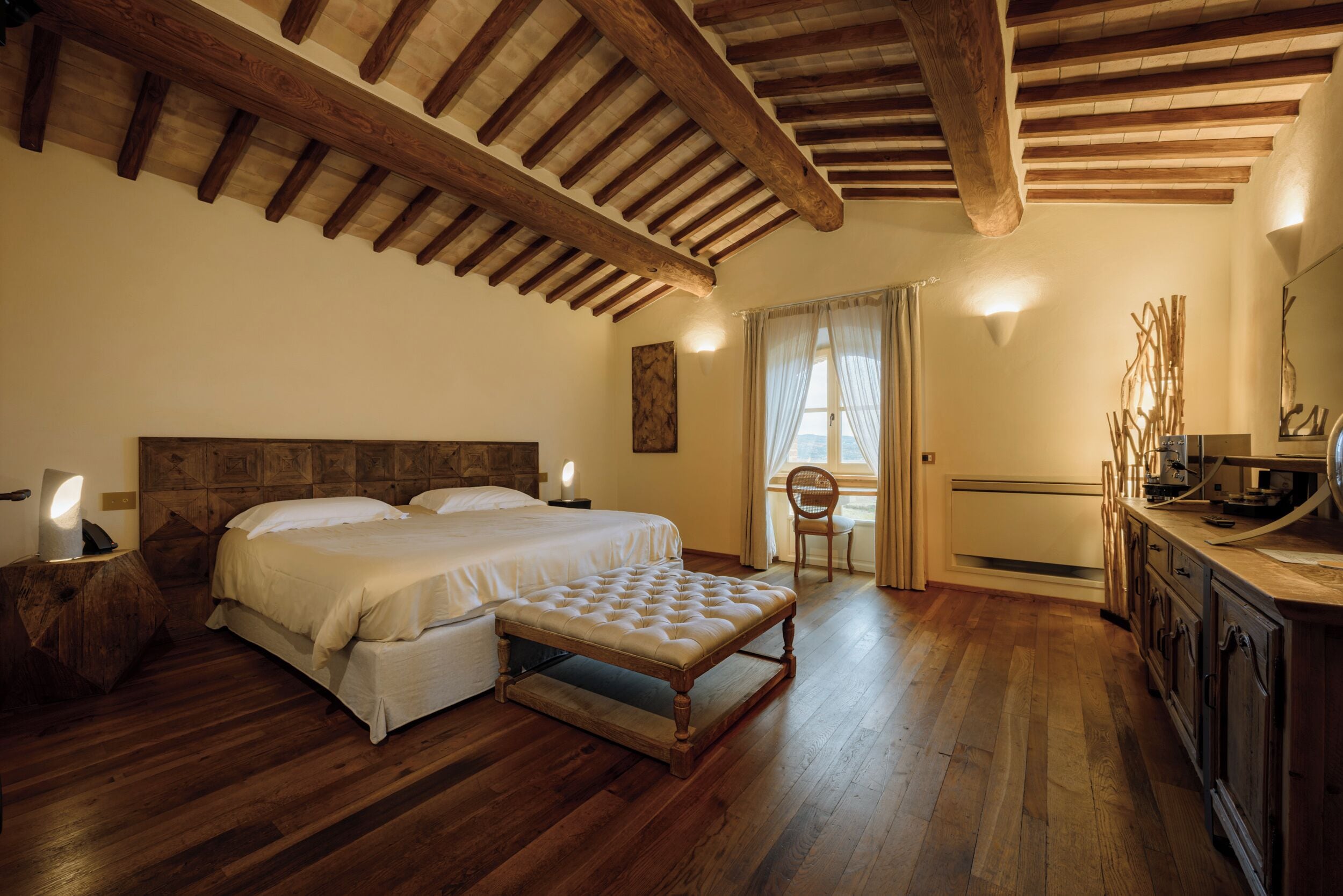 Un dormitorio con techo de madera, una cama grande, un banco, una mesita de noche y un aparador.