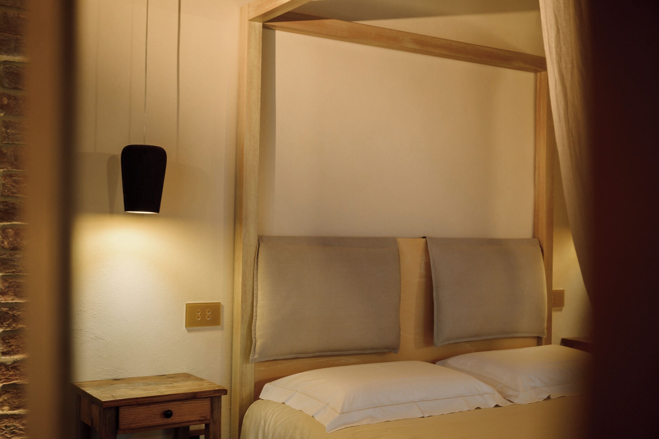 Un dormitorio con cabecera de madera, una mesita de noche con cajón y una lámpara fijada a la pared.