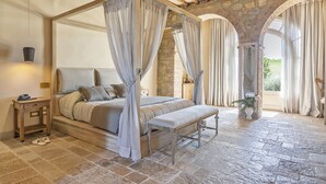 Una cama con dosel, un banco, suelo de piedra y pared de piedra.