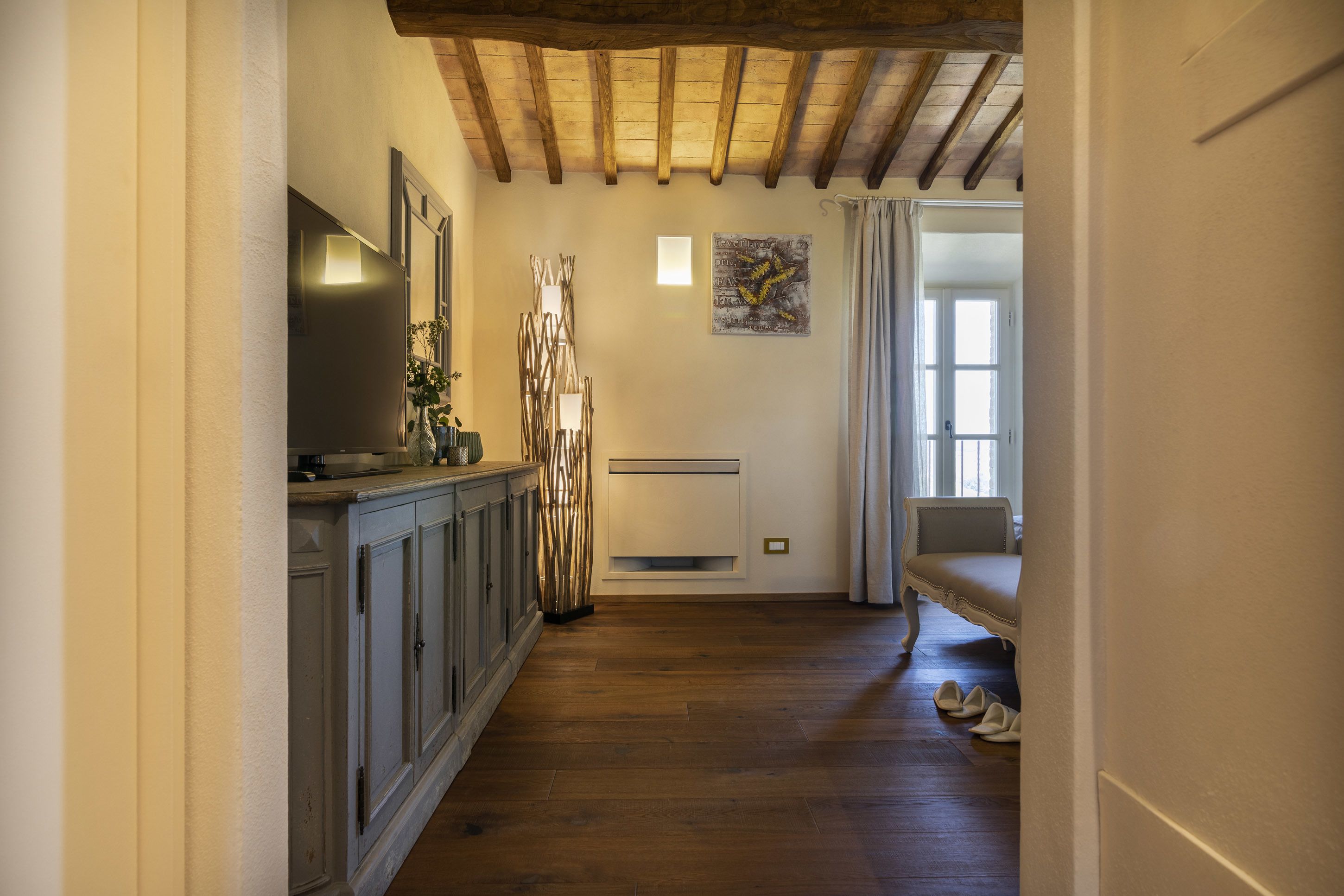 A hallway with wooden flooring, a cabinet with a flat-screen TV, a radiator, and a painting on the wall.