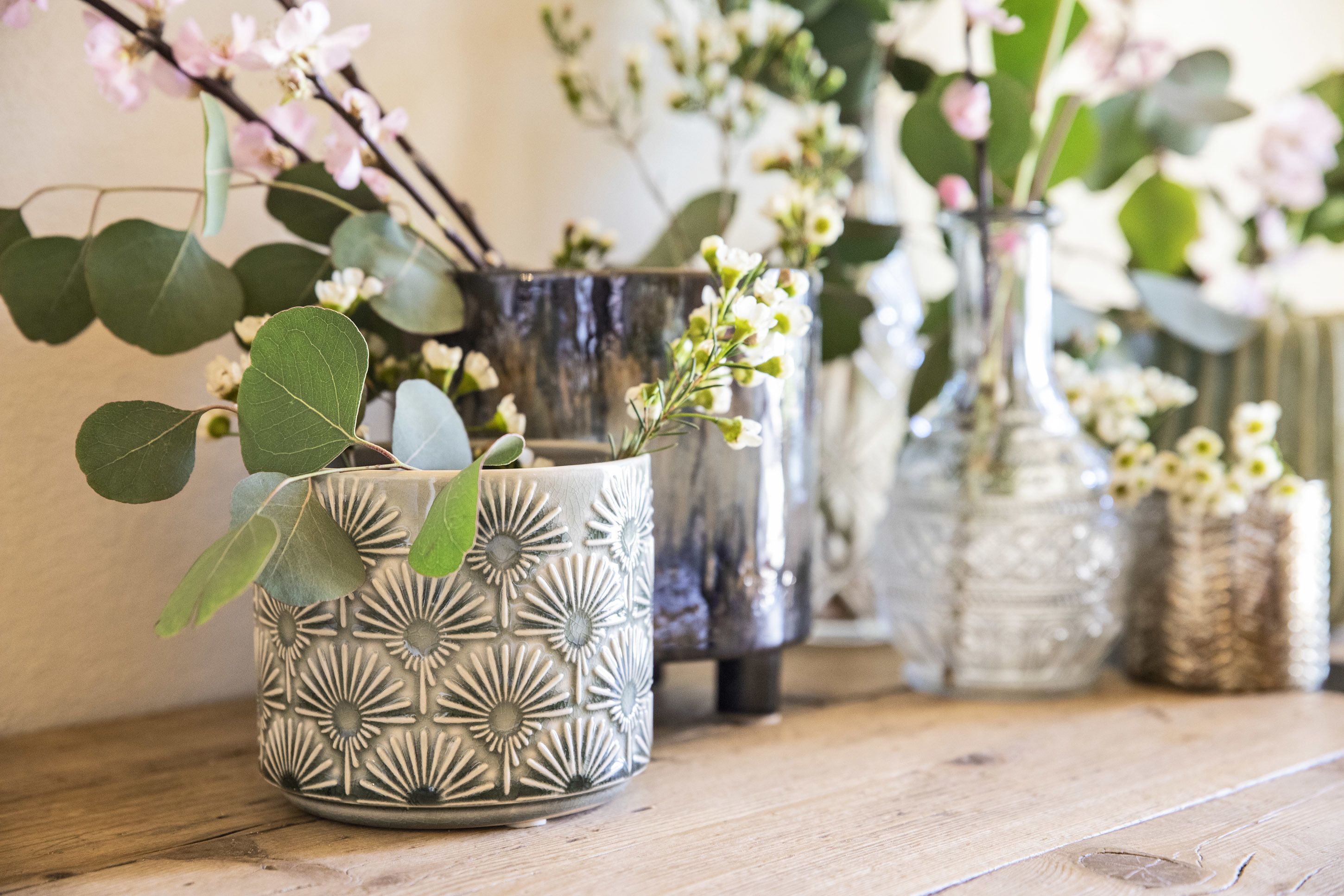 Una mesa de madera con jarrones decorativos que contienen flores y follaje.