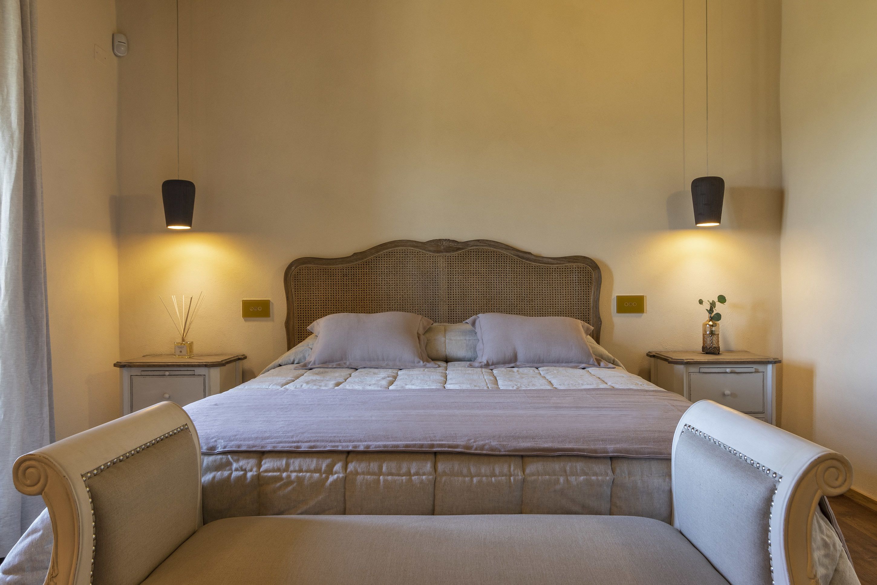 Un letto rifatto con cura, una testiera, due comodini con lampade e una sedia.