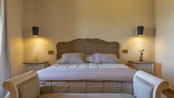 Un letto rifatto con cura, una testiera, due comodini con lampade e una sedia.