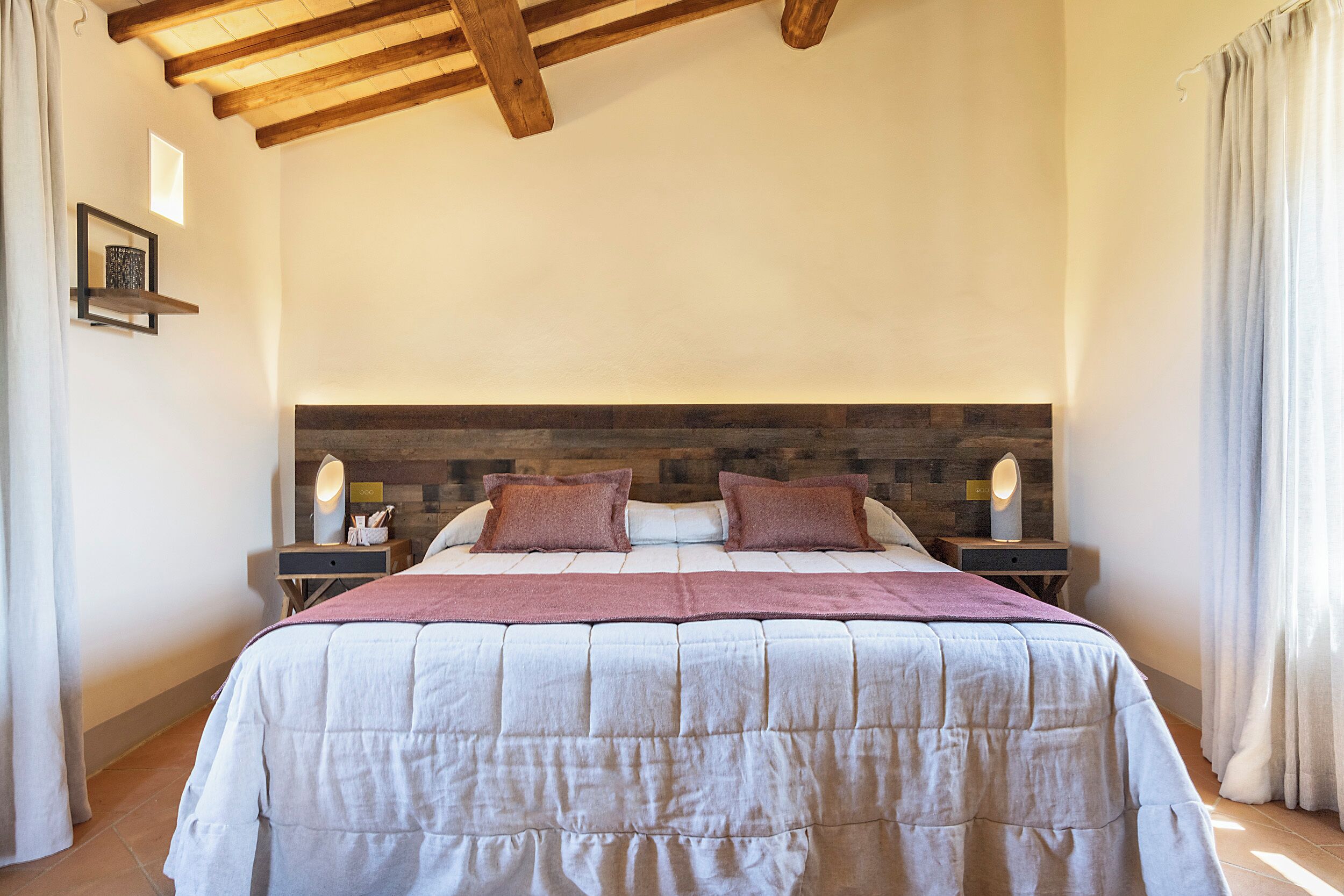 A bedroom with a large bed, wooden headboard, bedside tables with lamps, and a hanging light fixture.