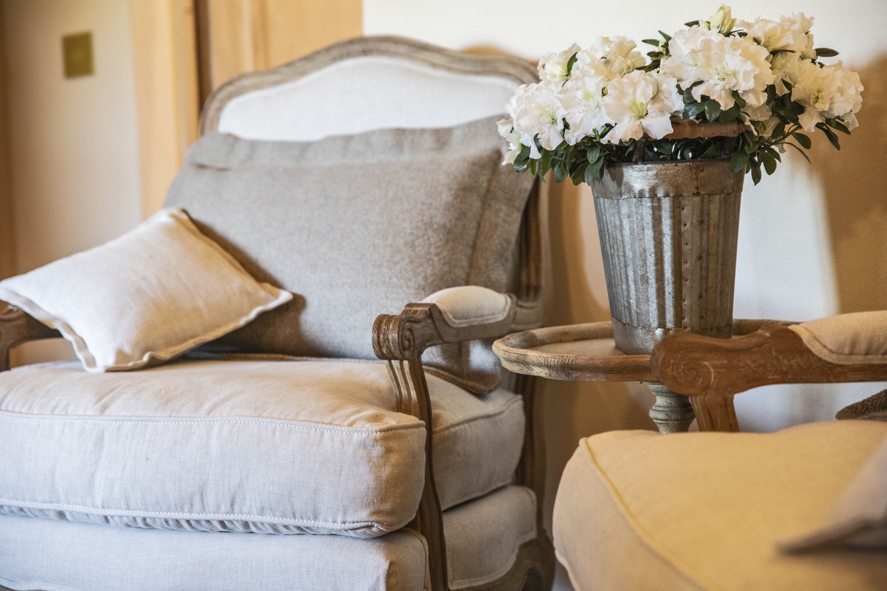 A classic armchair with a cushion, a small table with a vase of white flowers, and a matching pillow.