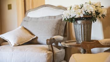 A classic armchair with a cushion, a small table with a vase of white flowers, and a matching pillow.