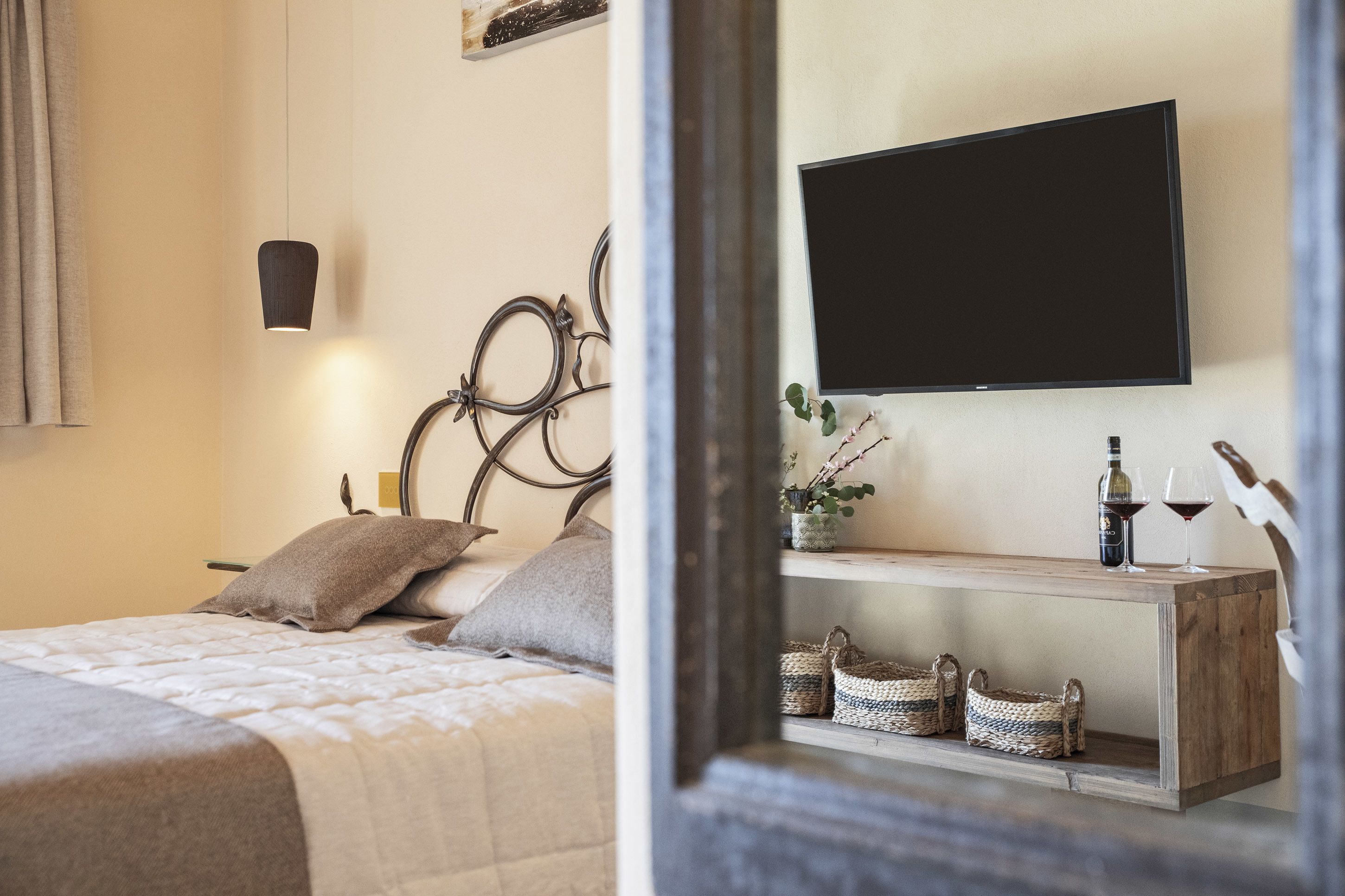 A neatly arranged bedroom with a bed, a bedside table with a bottle and glasses, and a mounted TV.