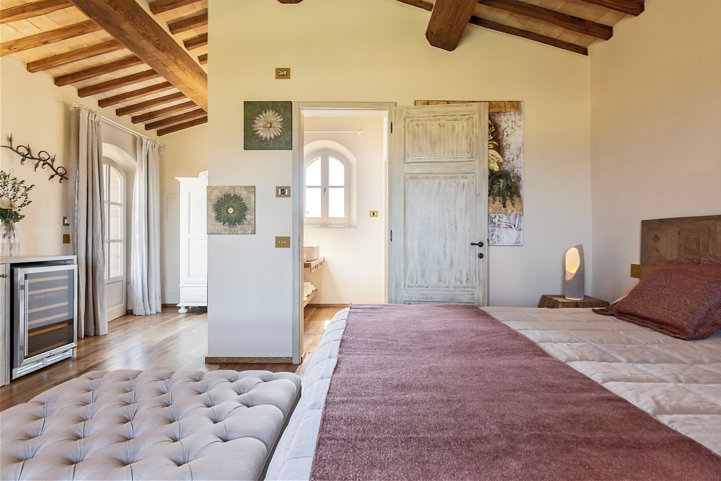 Een slaapkamer met een groot bed, een gestoffeerde bank, een houten plafond en een deur naar een andere kamer.