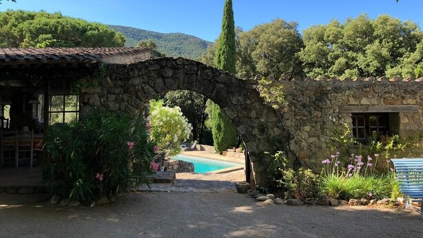A stone archway leading to a pool area surrounded by lush greenery and a mountain backdrop.