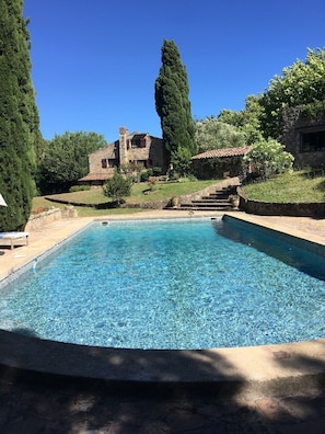 A rectangular swimming pool with clear blue water, surrounded by stone walls and greenery.