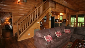 A wooden cabin interior with a staircase, a brown leather sofa with decorative pillows, and a foosball table. - Lakefront 3-bedroom cabin on Fontana Lake with stunning views and a private dock (Robbinsville)