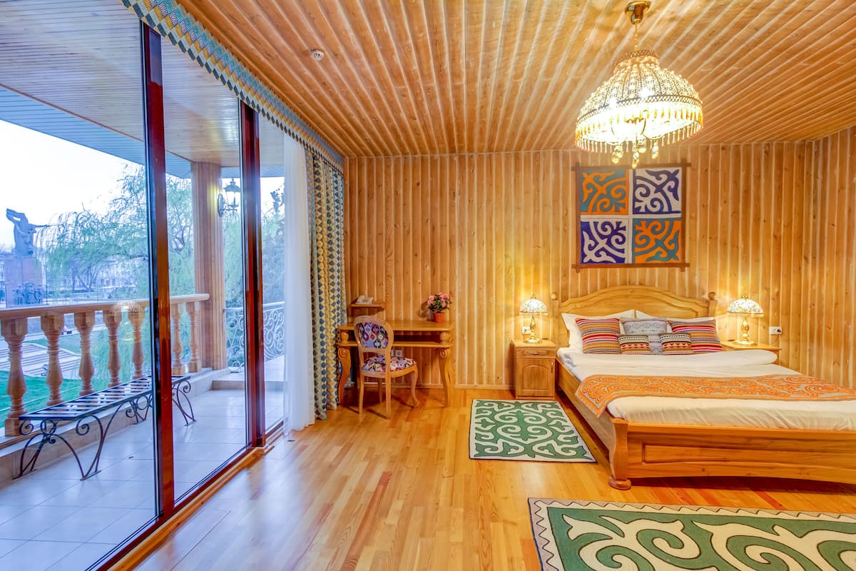 Ein Schlafzimmer mit Holzwandverkleidung, ausgestattet mit einem großen Bett, einem Schreibtisch und einem Stuhl. Ein Balkon mit Geländer bietet einen Blick ins Freie.
