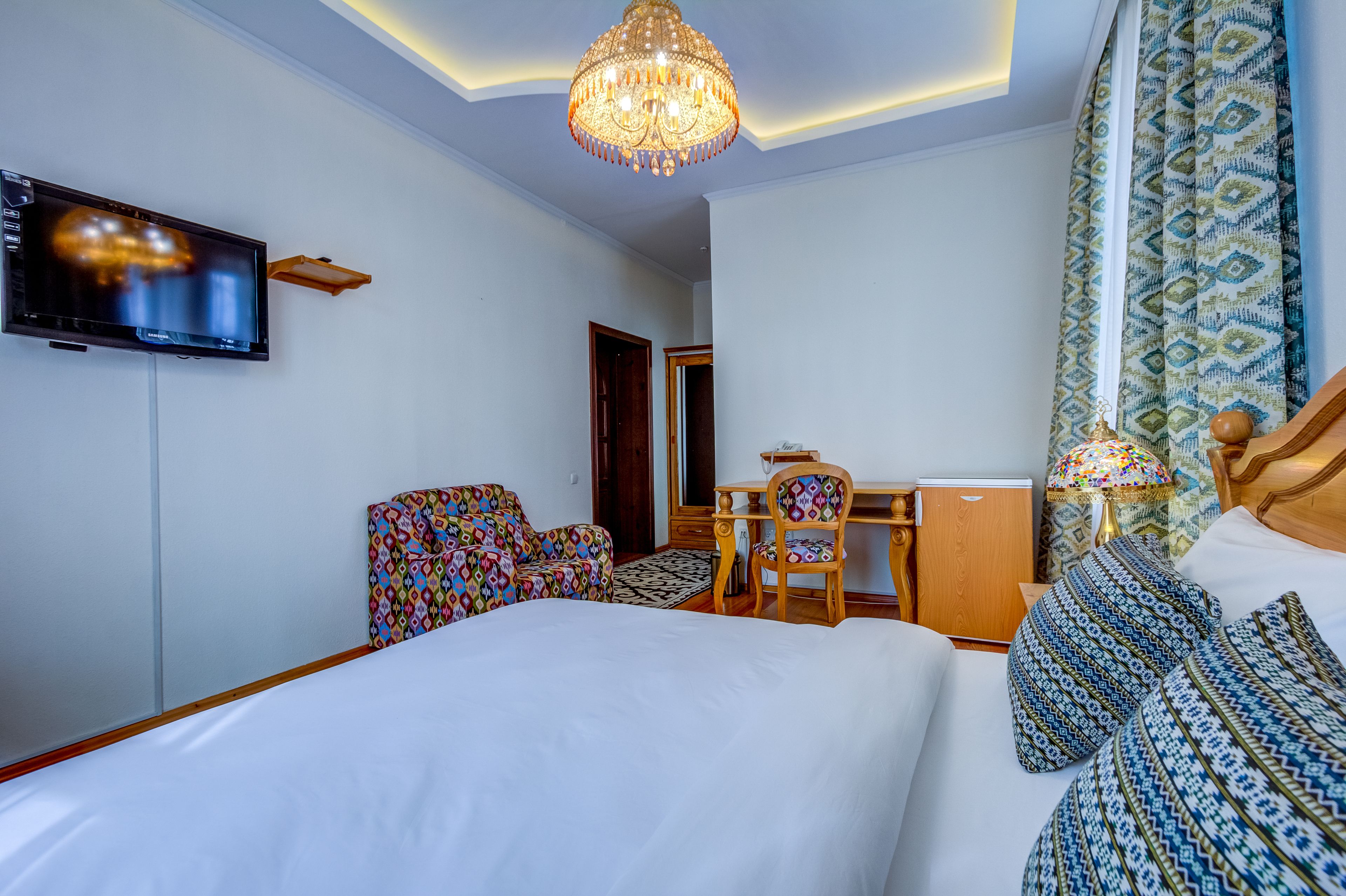 Habitación de hotel con una cama grande, un escritorio con silla, televisión y una araña.