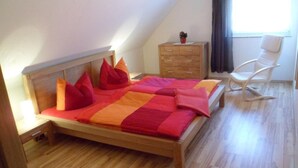 Un dormitorio con una cama de madera, un tocador de madera, una silla blanca y una ventana con cortinas.