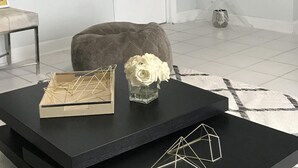 A modern living room with a black coffee table, a grey ottoman, and a vase with white flowers.