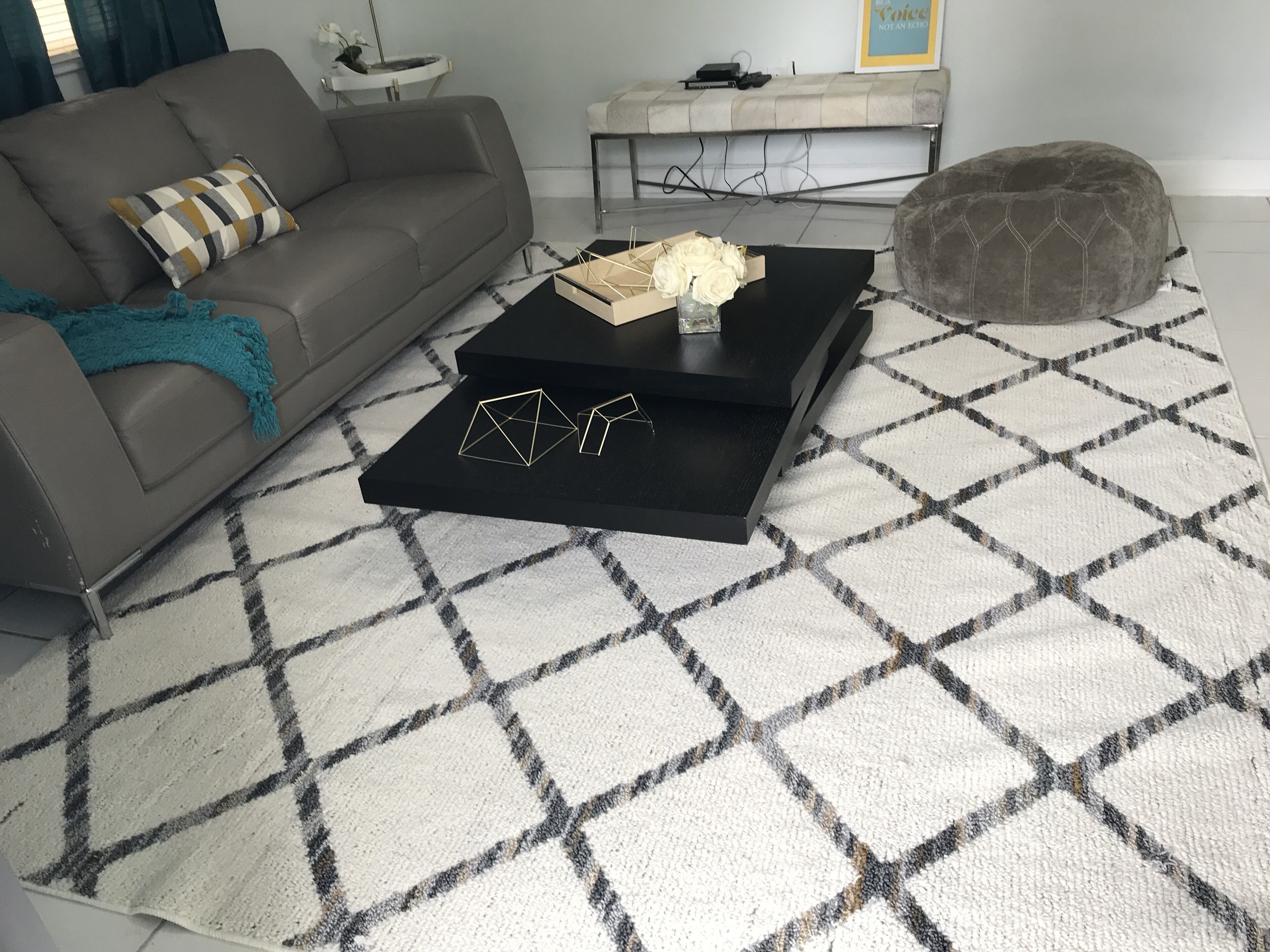 Sala de estar com sofá, mesa de centro, banquinho e tapete estampado.