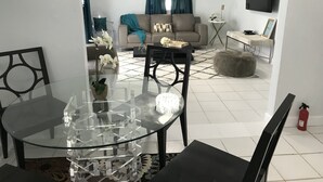 A modern living room with a glass dining table, a sofa, and a TV mounted on the wall.
