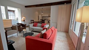 A living room with a red sofa, a grey sofa, and a coffee table. There is a dining table with chairs, a lamp, and a window with a view of the outside. - Le Duplex - Pontaly Farm (BAILLY)
