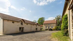 A building with a gravel courtyard, a stone wall, and a red-roofed structure in the background. - Le Duplex - Pontaly Farm (BAILLY)