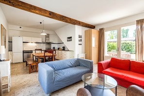 Una cocina moderna con armarios blancos, techo de madera y un área de comedor con un sofá azul y uno rojo.
