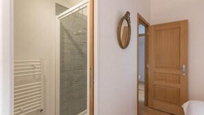 Een badkamer met een douche, een houten deur en een spiegel aan de muur.