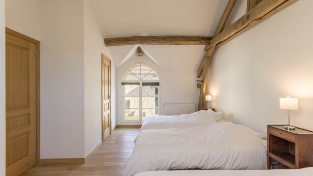 A bedroom with two beds, wooden beams, a window with a view, and a nightstand with a lamp. - Le Duplex - Pontaly Farm (BAILLY)