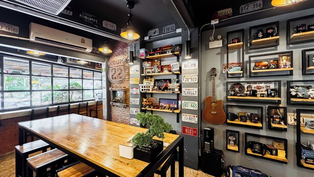 Interior de restaurante con una mesa de madera, sillas, una planta en maceta y una pared decorada con placas de matrícula y recuerdos.