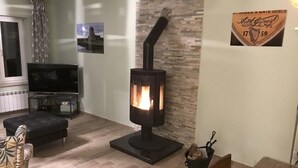 Una sala de estar con estufa de leña, televisor y comedor con mesa y sillas.