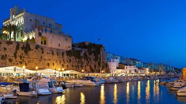 Un bâtiment historique doté d’une tour, un port de plaisance avec des bateaux et un restaurant situé au bord de l’eau.