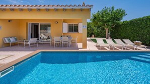 Un espace aménagé au bord de la piscine, avec un bâtiment jaune, des sièges extérieurs et une piscine à l’eau d’un bleu limpide.
