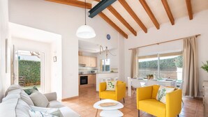 Un grand espace de vie comprenant un canapé, des fauteuils jaunes et une table à manger. On aperçoit une cuisine au fond.