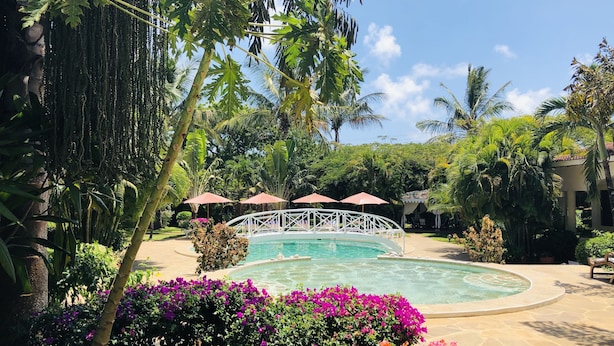 A pool surrounded by tropical plants and a white bridge. - Hotel Villa Malindi (Malindi)