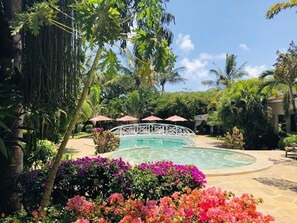 Una piscina rodeada de plantas tropicales y un puente blanco.
