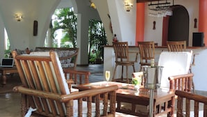 A spacious indoor area with wooden furniture, including chairs and a table, and a bar area with a wine rack. - Hotel Villa Malindi (Malindi)