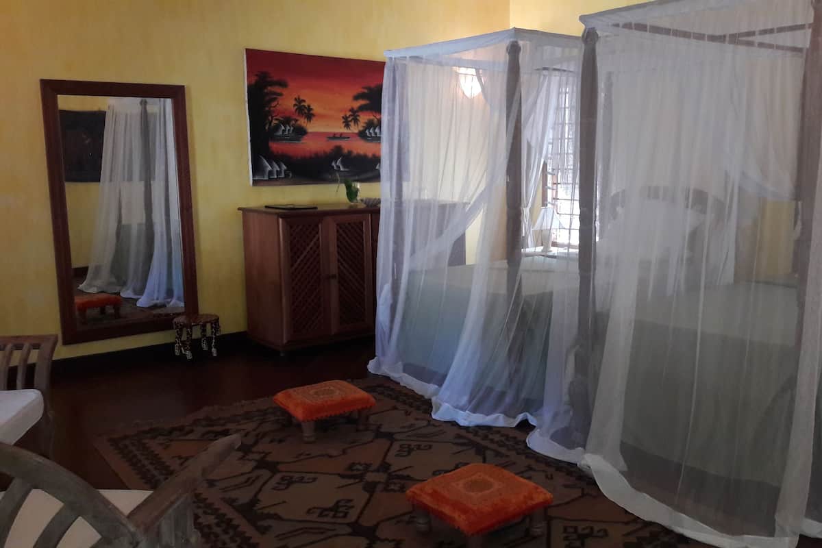 A room with a bed, a wooden cabinet, a painting, and a window with a view of palm trees.