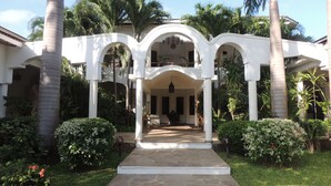 A covered outdoor area with a stone pathway leading to a seating area, surrounded by palm trees and greenery. - Hotel Villa Malindi (Malindi)