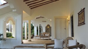 A spacious indoor area with a wooden bench, a table, and a chair. There are columns and a door in the background. - Hotel Villa Malindi (Malindi)