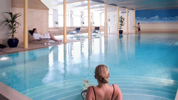Une piscine intérieure à l’eau d’un bleu limpide, dotée de chaises longues et agrémentée de plantes en pot.