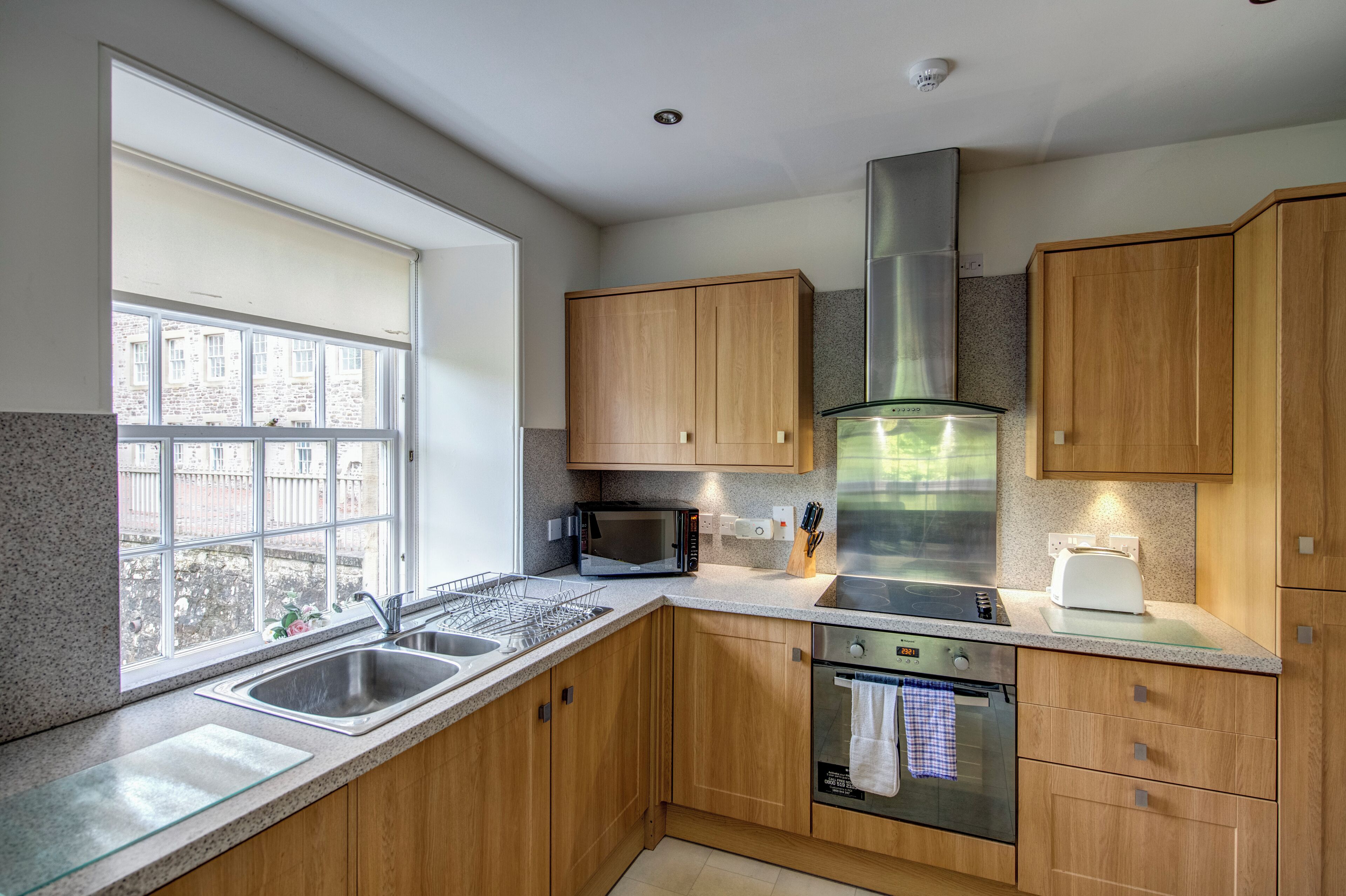 A modern kitchen with wooden cabinets, a stainless steel range hood, a microwave, a toaster, and a dishwasher.