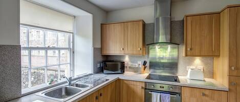 A modern kitchen with wooden cabinets, a stainless steel range hood, a microwave, a toaster, and a dishwasher.